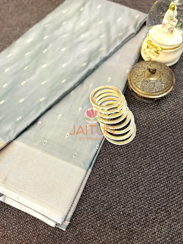 Elegant Grey Banarasi Silk Saree flatlay featuring delicate silver zari motifs, classic chevron border, and contemporary styling with gold bangles