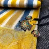 Mustard & Blue Striped Chiniya Silk Saree with statement jewelry placed on floral border and striped pattern