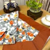 Amber Floral Bloom bed sheet set featuring orange and yellow floral print with solid brown border, styled on a table setting