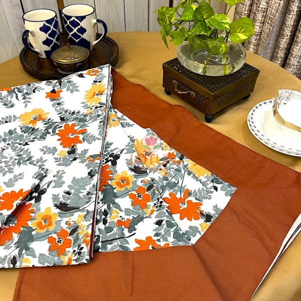 Amber Floral Bloom bed sheet set featuring orange and yellow floral print with solid brown border, styled on a table setting