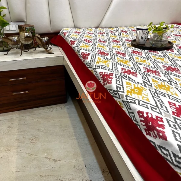 Angled display of Ikat Harmony bed sheet with elegant maroon and mustard ikat patterns, styled in a contemporary bedroom.