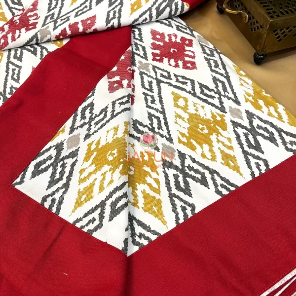 Ikat Harmony bed sheet showing rich maroon border and intricate mustard, grey, and red ikat pattern at the corner detail.
