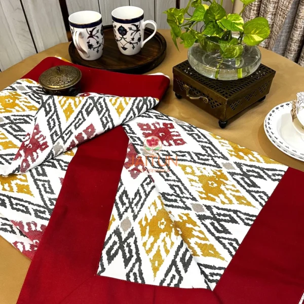 Ikat Harmony bed sheet set with maroon border, mustard and red ikat pattern, styled with tableware and decor for an elegant look.