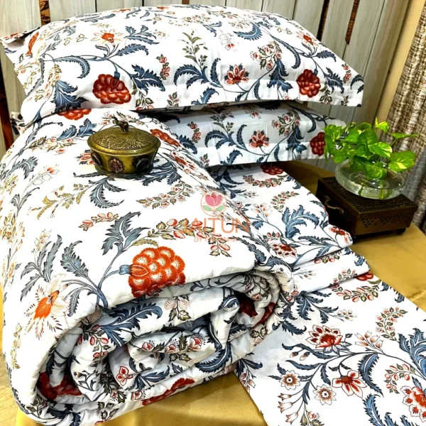 Royal Crimson Bloom cotton bed sheet set with floral-patterned pillows and quilt in deep crimson and blue, showcased with a decorative brass box.