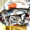 Closeup of Royal Crimson Bloom cotton bed sheet set featuring a rolled quilt with elegant crimson floral and blue leaf prints.