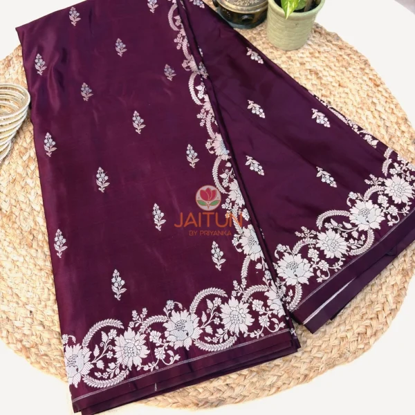 Folded deep wine Banarasi silk saree with silver zari floral border and pallu detailing.